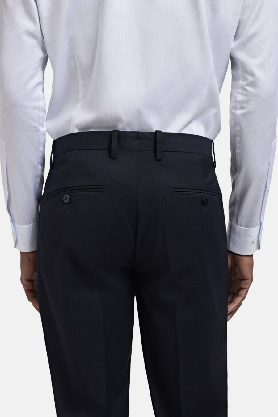 Achterkant van een persoon in een blauw gestreept overhemd en donkerblauwe pantalon.