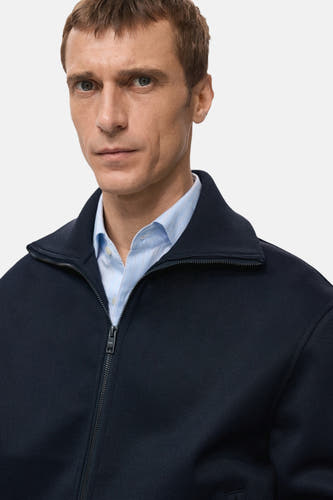 Gilet bleu de MANGO porté sur un chemisier rayé bleu clair.