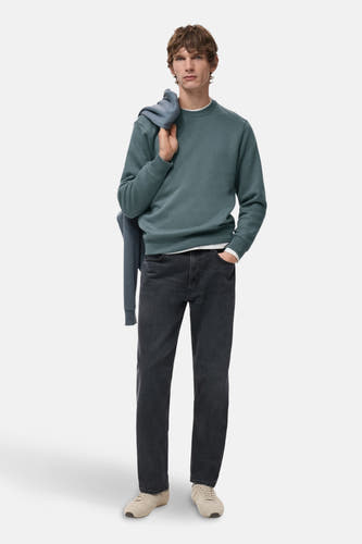 Pull-over bleu avec col rond de MANGO, porté avec un autre pull-over sur l'épaule et des jeans foncés.