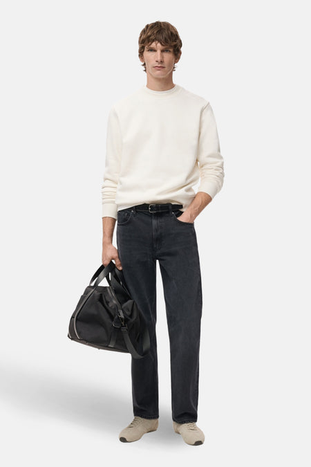 Man in crèmekleurige sweater, zwarte jeans, beige sneakers met een zwarte tas.