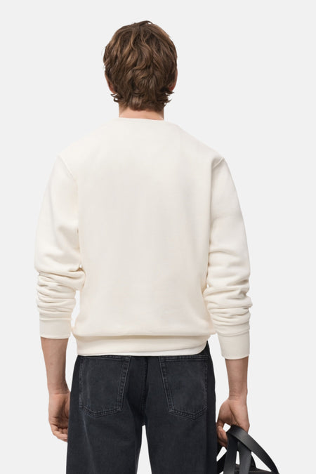 Man met rug naar camera in gebroken witte trui en zwarte jeans.