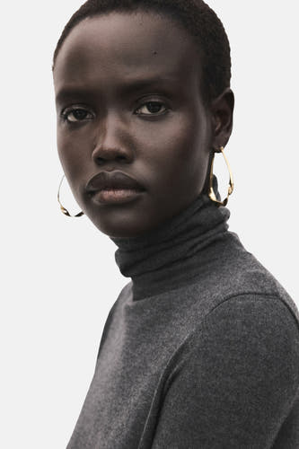 Sweat-shirt gris à col rond de MANGO, avec une fine texture côtelée et des boucles d'oreilles dorées.