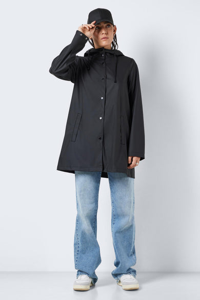 Manteaux de pluie noirs de DROPLETS, avec capuche, longues manches, fermeture à boutons et portés avec un jean bleu et des baskets blanches.