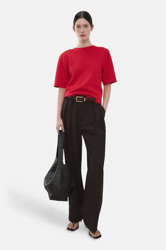 Pull rouge à col rond de MANGO, porté avec un pantalon marron, une ceinture et des sandales noires, avec un sac à main noir.