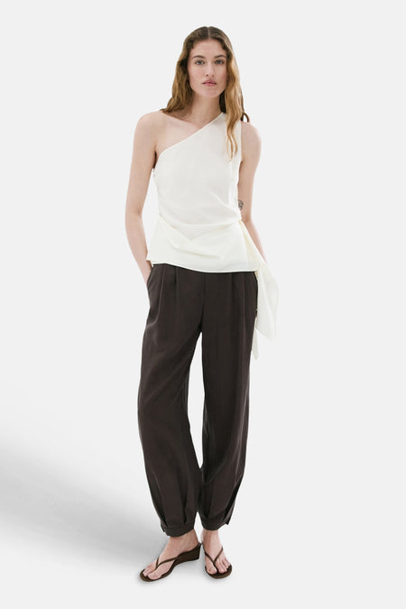 Chemisier blanc asymétrique de MANGO avec devant drapé, combiné avec un pantalon foncé et des sandales.
