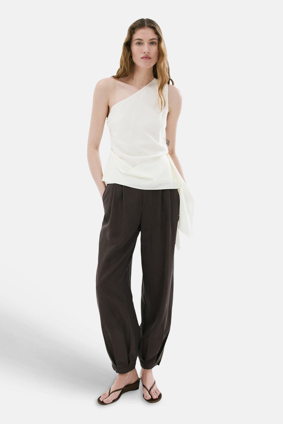 Chemisier blanc asymétrique de MANGO avec devant drapé, combiné avec un pantalon foncé et des sandales.