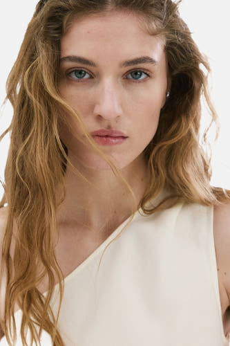 Chemisier blanc sans manches MANGO à une épaule, porté par un mannequin aux longs cheveux blonds.