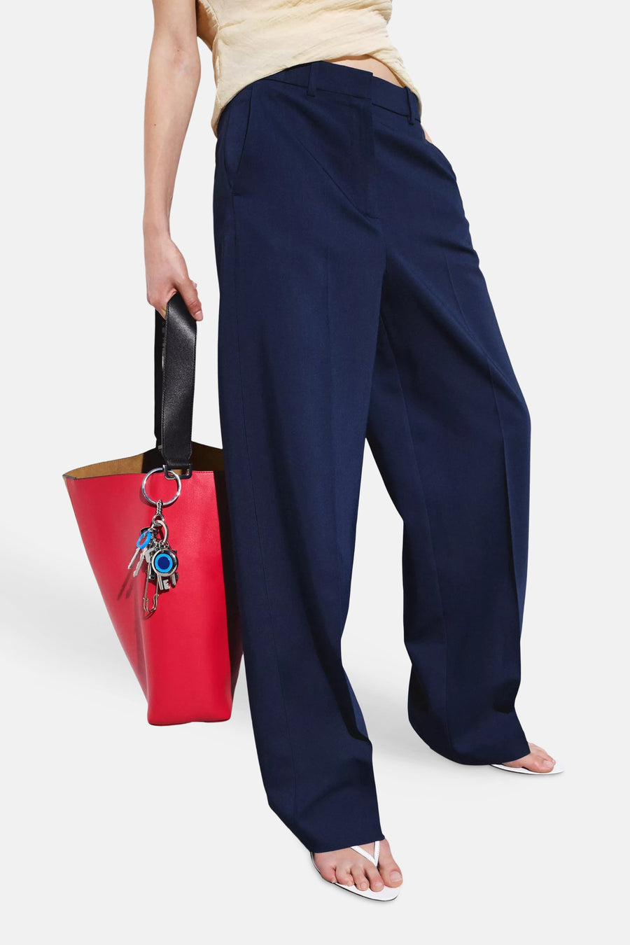 Pantalons de costume bleus de MANGO, à jambes larges, portés avec un haut décolleté couleur crème et un sac rouge, vus de dos.