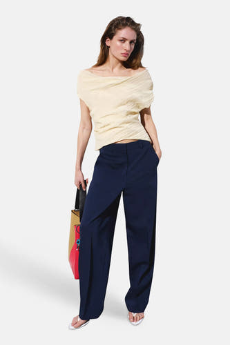 Pantalon de costume bleu de MANGO à jambes larges, porté par un mannequin avec un haut crème et un sac multicolore.