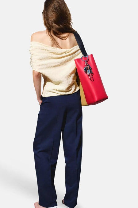 Blauwe kostuumbroeken van MANGO, met wijde pijpen, gedragen met crèmekleurige off-shoulder top en rode tas, vanaf de achterkant.