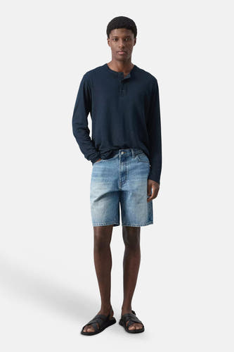 Bermuda en denim bleu moyen de MANGO, porté avec un t-shirt Henley bleu foncé et des sandales noires.