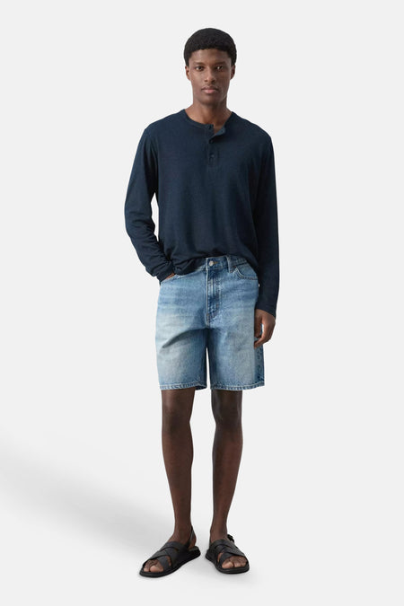 Bermuda en denim bleu moyen de MANGO, porté avec un t-shirt Henley bleu foncé et des sandales noires.