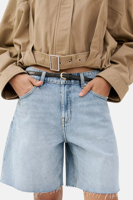 Bermuda en jean bleu clair de MANGO avec ourlet brut, combiné avec une chemise marron et une ceinture chaîne dorée, vue de dos.