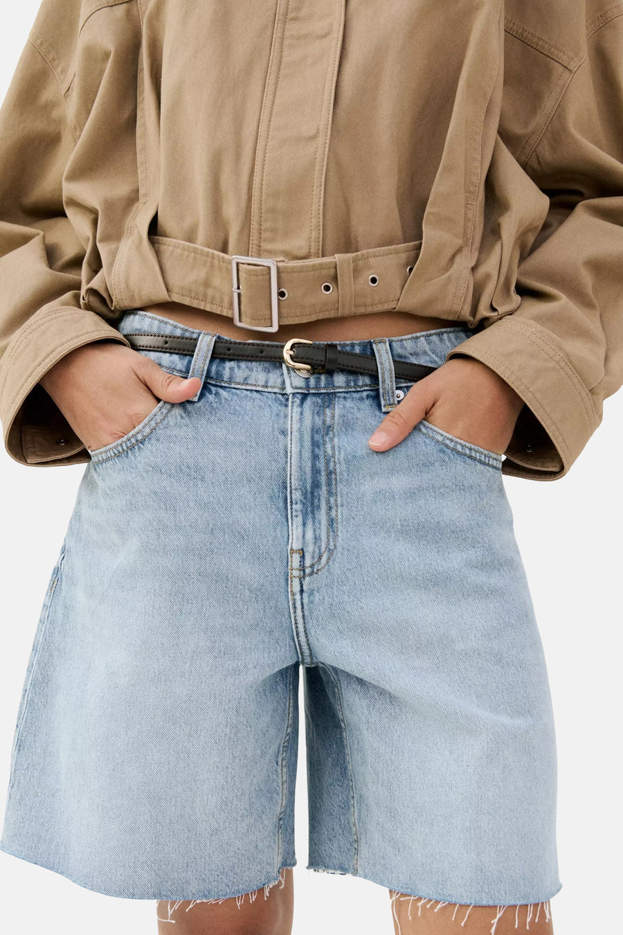 Bermuda en jean bleu clair de MANGO avec ourlet brut, combiné avec une chemise marron et une ceinture chaîne dorée, vue de dos.