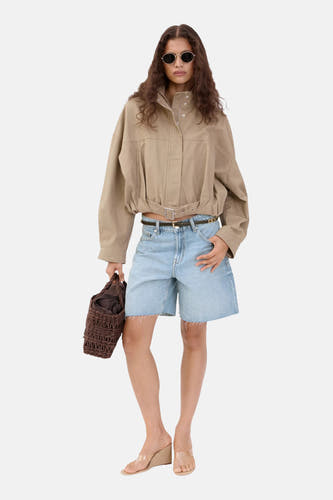 Bermuda en jean bleu clair de MANGO avec jambes larges et ourlet effiloché, portés avec une veste beige et des sandales claires.