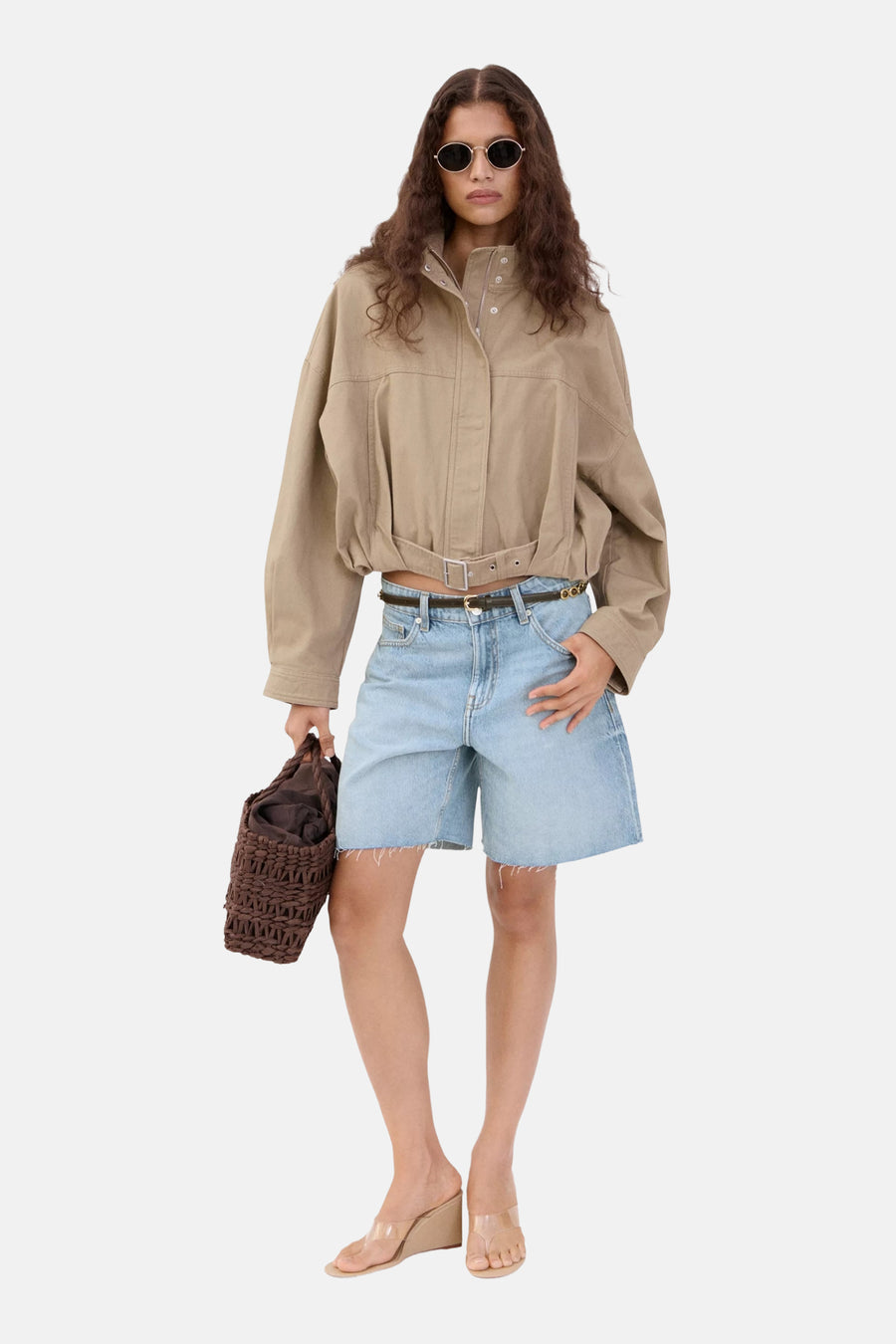 Bermuda en jean bleu clair de MANGO avec jambes larges et ourlet effiloché, portés avec une veste beige et des sandales claires.