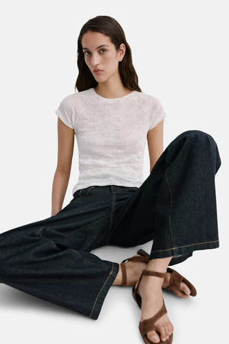 Beige korte mouwen t-shirt van MANGO, gebreid met ronde hals, gedragen met donkere wijde jeans en bruine sandalen, lifestyle shot.
