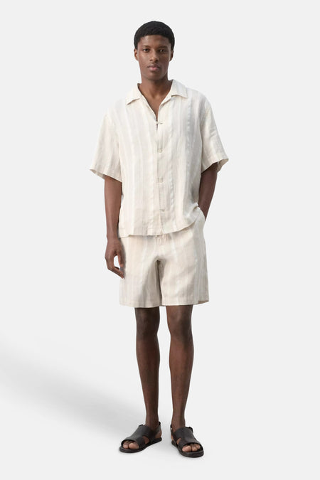 Bermuda beige à rayures de MANGO avec des rayures verticales, porté avec une chemise assortie et des sandales.