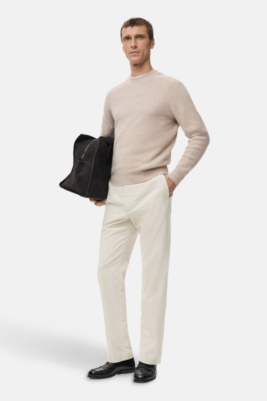 Jean écru de MANGO, porté avec un pull beige et des chaussettes noires, tenant un sac à la main.