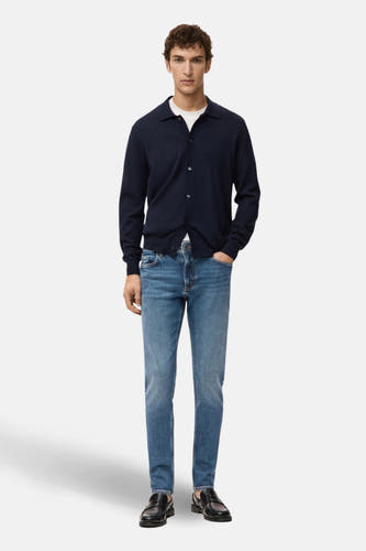 Jean slim fit bleu de MANGO porté avec un veston bleu marine, un T-shirt blanc et des chaussures noires.