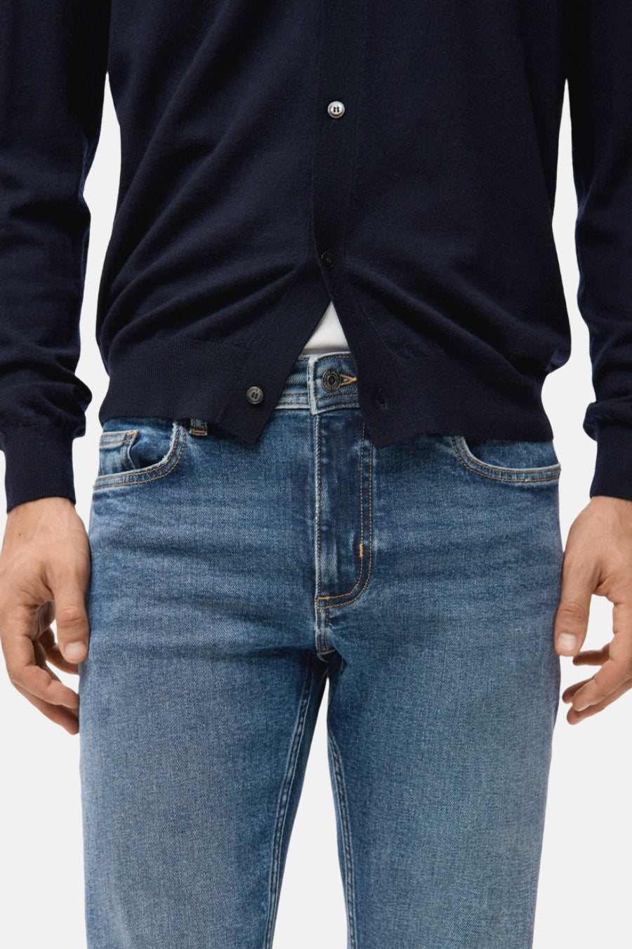 Jean slim en denim bleu moyen de MANGO, avec des coutures discrètes et porté avec un gilet bleu marine.