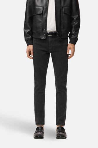 Man in zwarte jeans en leren jas met loafers.
