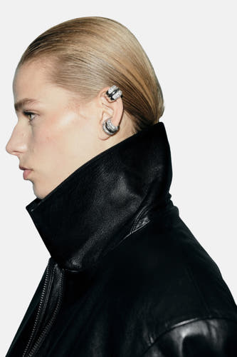 Boucles d'oreilles en argent de MANGO, portées à l'oreille en combinaison avec une veste en cuir à grande col.