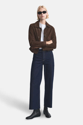 Jean bleu marine large de MANGO, associé à un manteau en daim brun et des bottines noires.