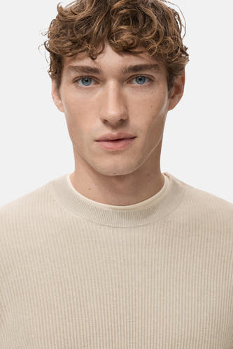 Gilet beige à col rond de MANGO, avec une texture côtelée et des manches longues.