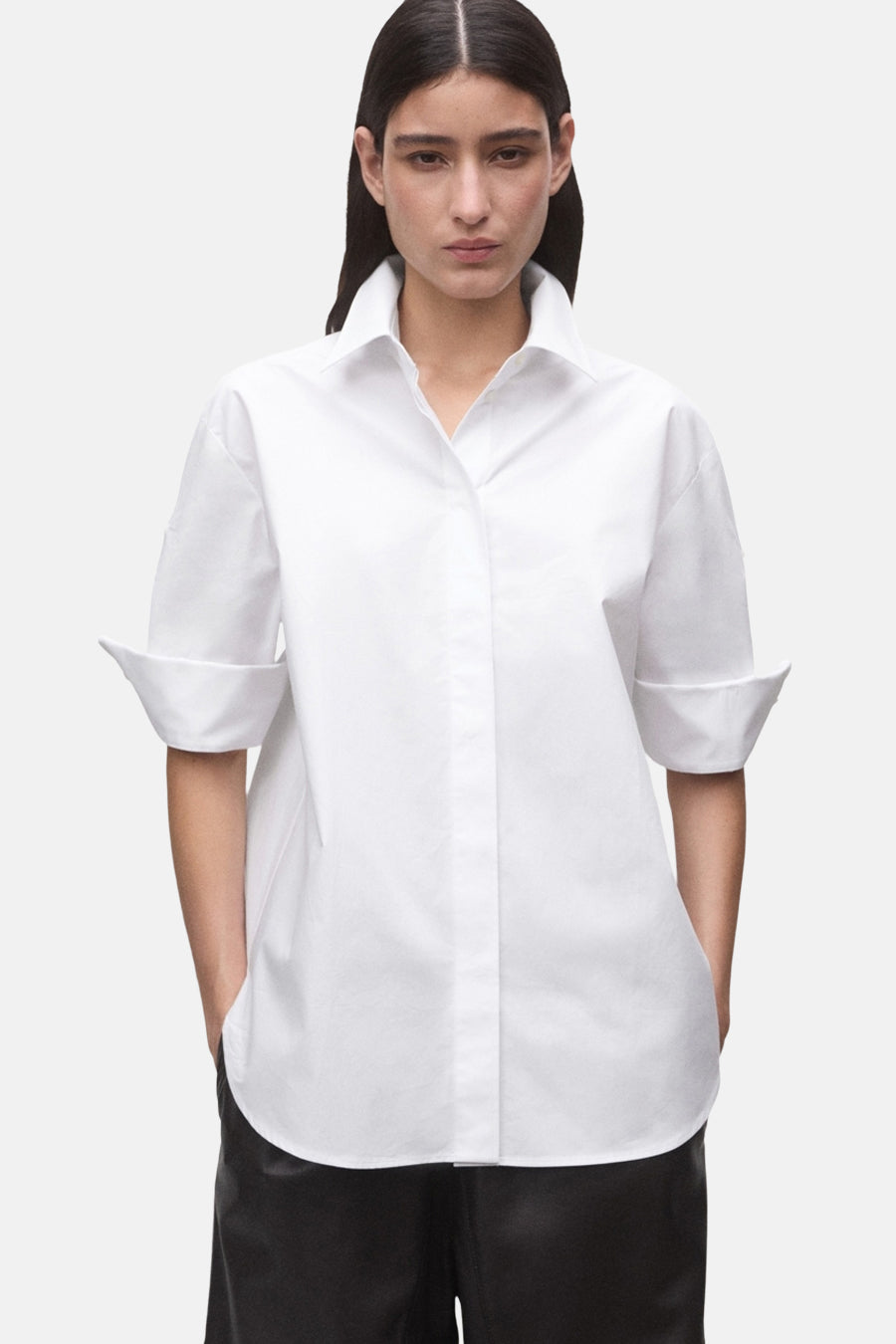 Chemise blanche à manches courtes de MANGO, avec manches retroussées et col classique, portée avec un pantalon noir.