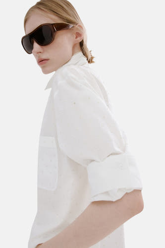 Chemise blanche à manches longues de MANGO, vue de dos, associée à un pantalon blanc et une queue de cheval.