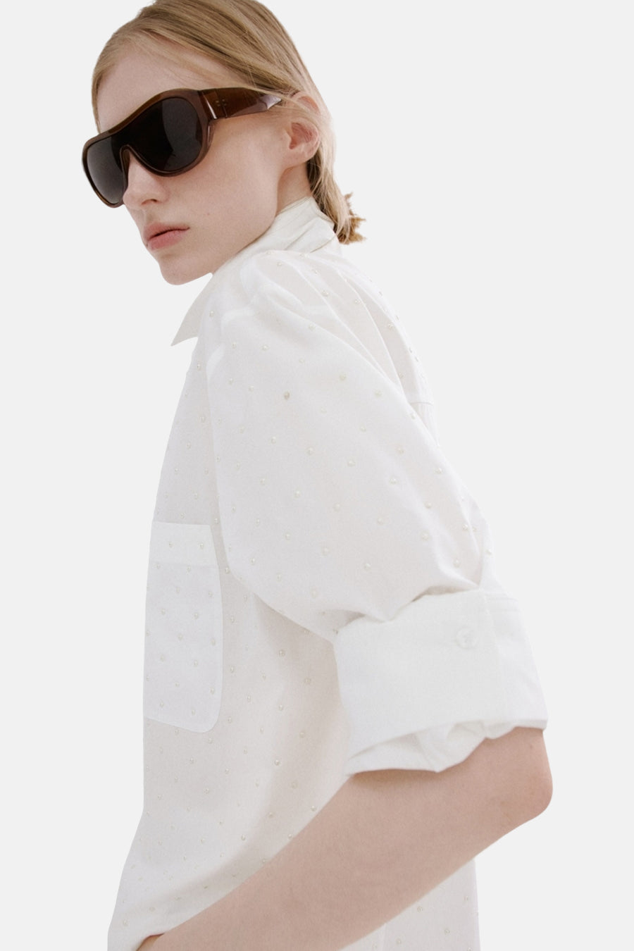 Chemise blanche à manches longues de MANGO, vue de dos, associée à un pantalon blanc et une queue de cheval.