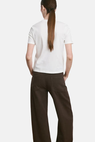 Wit T-shirt van MANGO, gezien van achteren, gecombineerd met een losse donkerbruine broek.