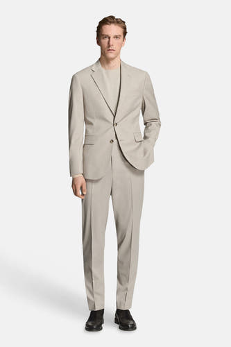 Blazer beige de MANGO, avec une fermeture à boutons et des poches, combiné avec un pantalon assorti et un T-shirt de la même couleur.