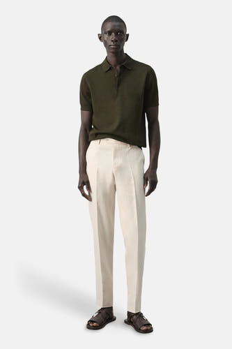 Polo verte de MANGO, portée avec un pantalon en lin de couleur crème et des sandales marron.