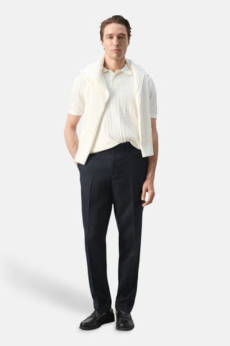 Polo blanche MANGO à motif torsadé et manches courtes, portée avec un pull sur les épaules et un pantalon foncé.