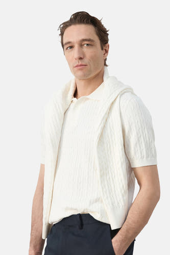 Polo blanche de MANGO, à manches courtes et à motif torsadé, portée avec un pull sur les épaules.