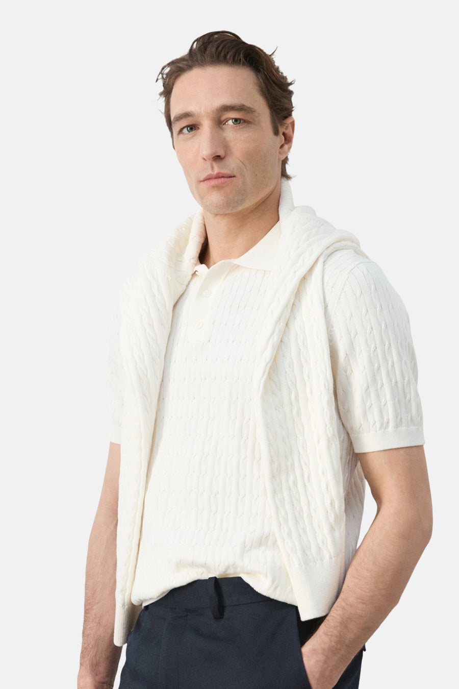 Polo blanche de MANGO, à manches courtes et à motif torsadé, portée avec un pull sur les épaules.