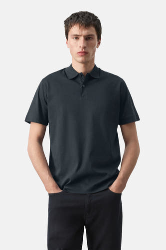 Polo bleue de MANGO, à manches courtes, vue de dos et associée à un pantalon noir.