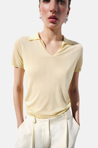 Polo jaune à manches courtes de MANGO, portée par un mannequin de dos, associée à un pantalon blanc cassé et des tongs rouges.