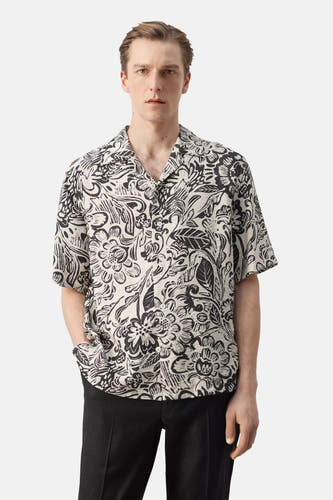 Chemise multicolore à manches courtes de MANGO avec motif floral noir et blanc, vue de dos avec un pantalon noir.
