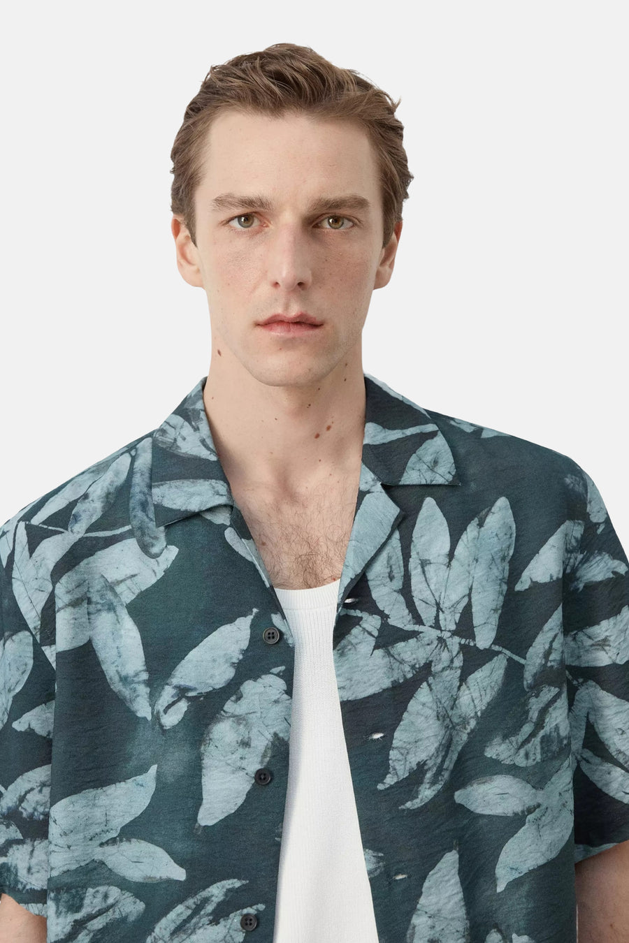 Chemise courte à manches courtes vert foncé avec motif de feuilles claires de MANGO, portée sur un débardeur blanc à col ouvert.