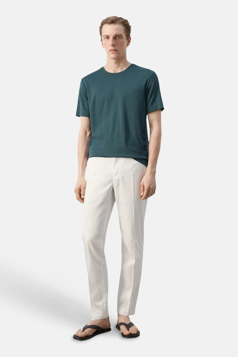 T-shirt vert à manches courtes de MANGO, avec col rond, combiné avec un pantalon clair et des tongs noires.
