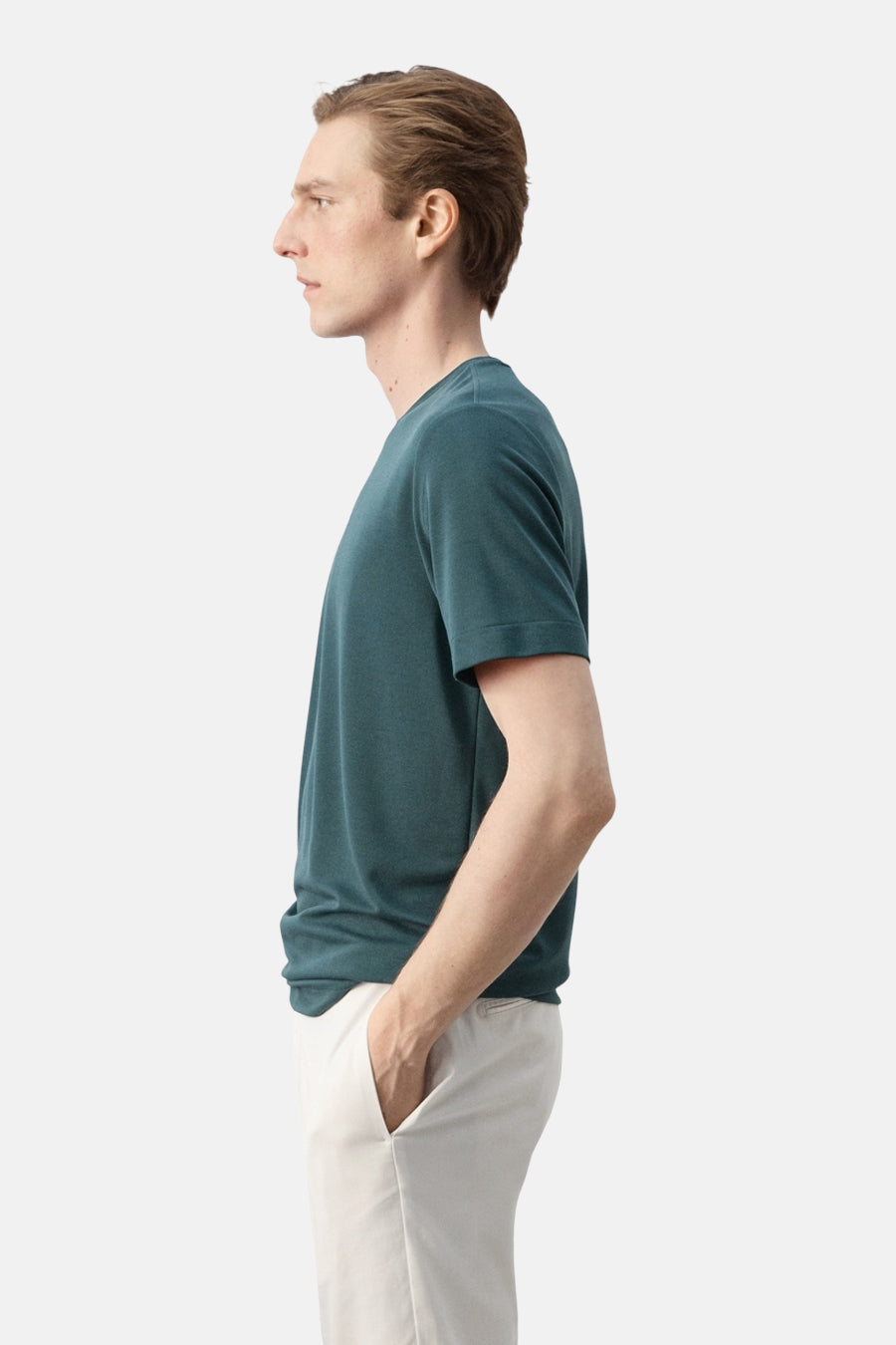 T-shirt vert à manches courtes de MANGO, porté par un homme avec les mains dans les poches d'un pantalon clair, vue de profil.