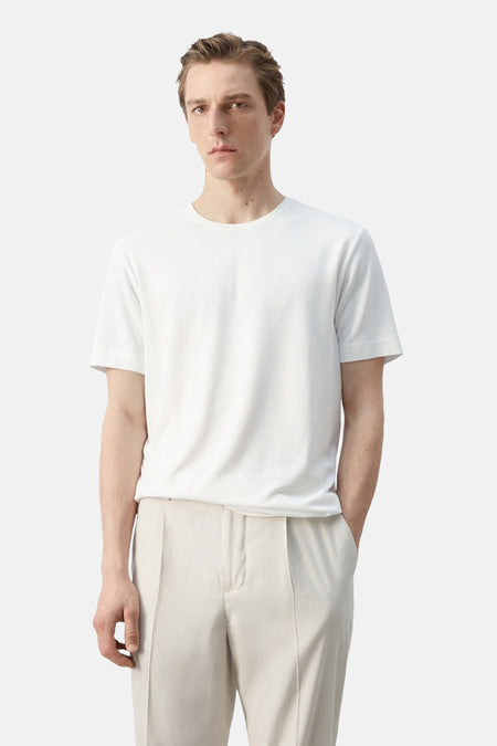 T-shirt blanc à manches courtes de MANGO, porté par un homme de profil avec un pantalon clair.