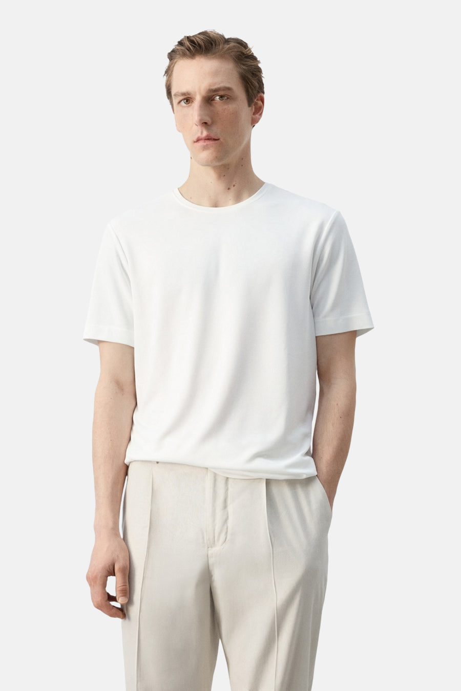 T-shirt blanc à manches courtes de MANGO, porté par un homme de profil avec un pantalon clair.