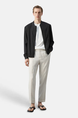 T-shirt blanc à manches courtes de MANGO, porté sous un bomber foncé avec un pantalon clair et des sandales.