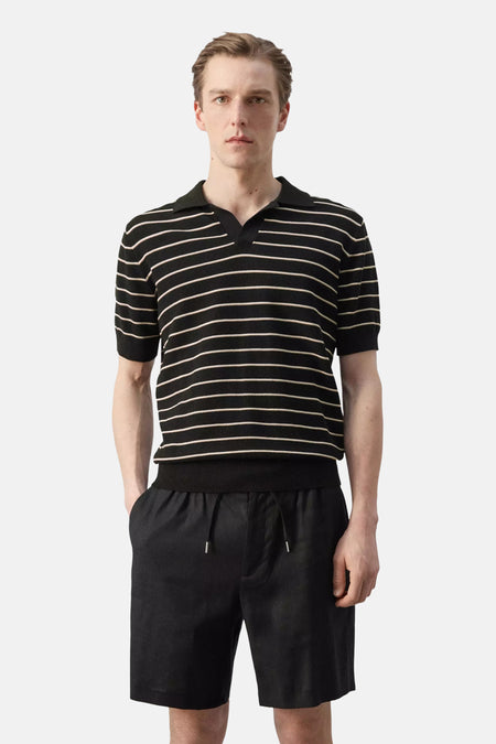 Polo noire de MANGO avec de fines rayures horizontales claires, manches courtes et col, vue de dos portée avec un short noir.