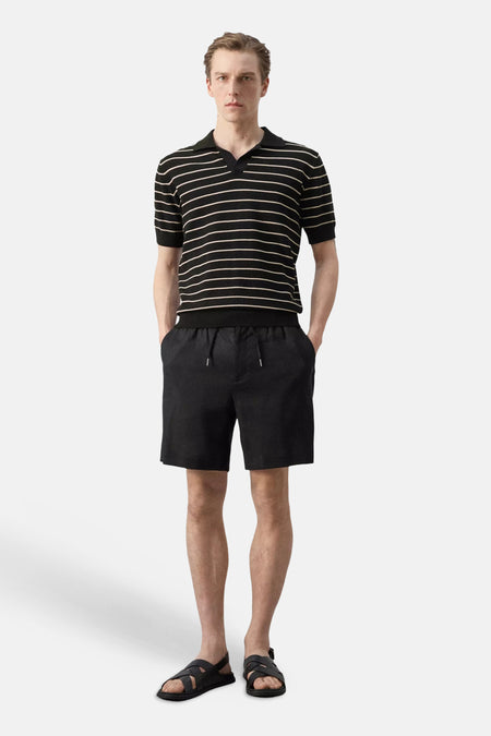 Polo noire MANGO à rayures horizontales beiges, col en V ouvert et manches courtes, portée avec un short noir et des sandales.