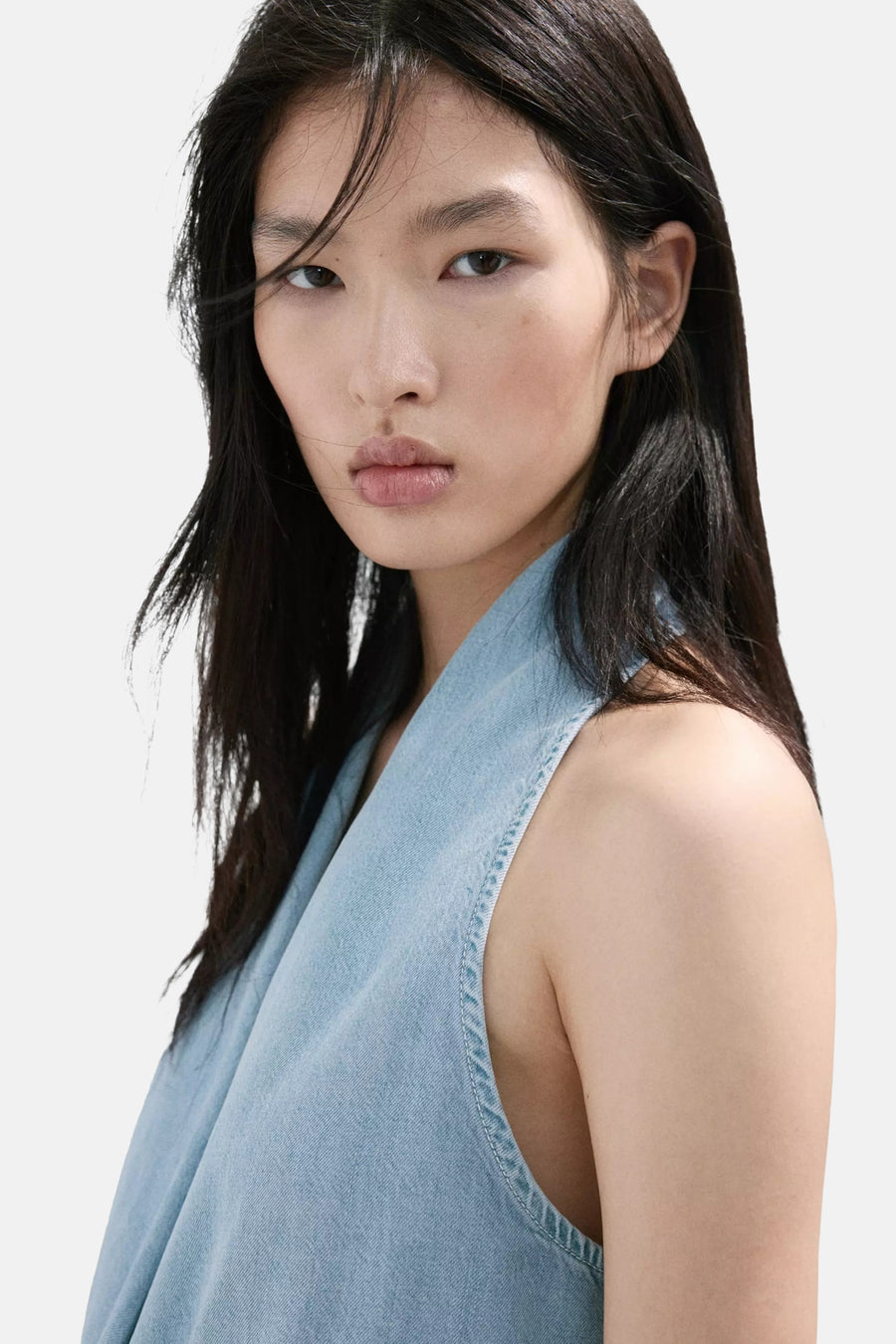 Lichtblauwe denim blouse zonder mouwen van MANGO, asymmetrische halslijn, close-up van model